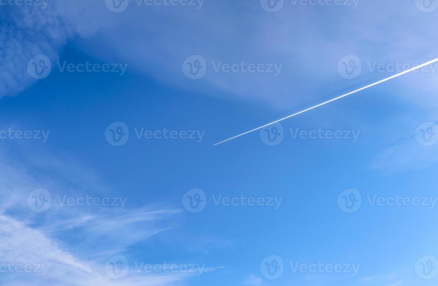 Aircraft condensation contrails in the blue sky inbetween some clouds photo