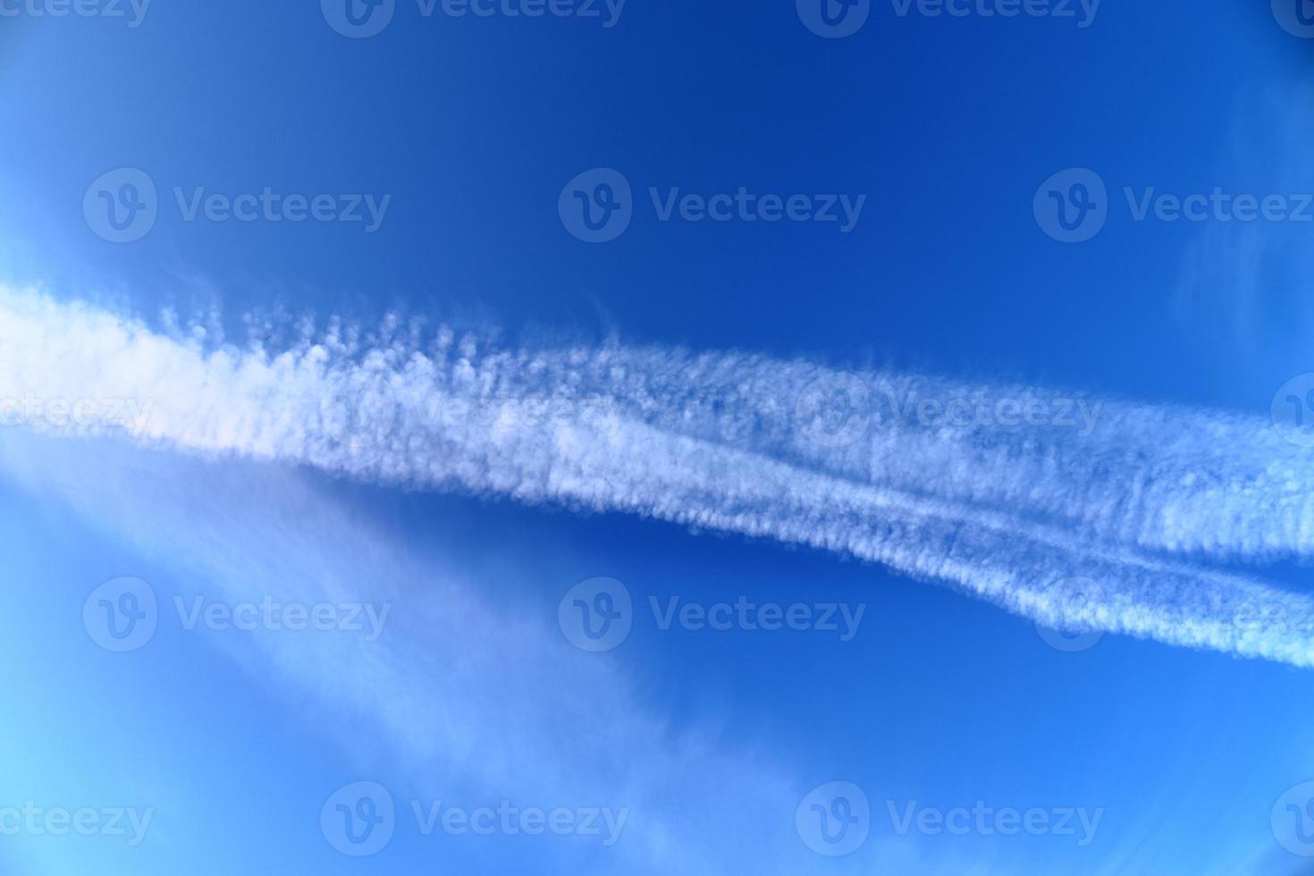 Aircraft condensation contrails in the blue sky inbetween some clouds photo