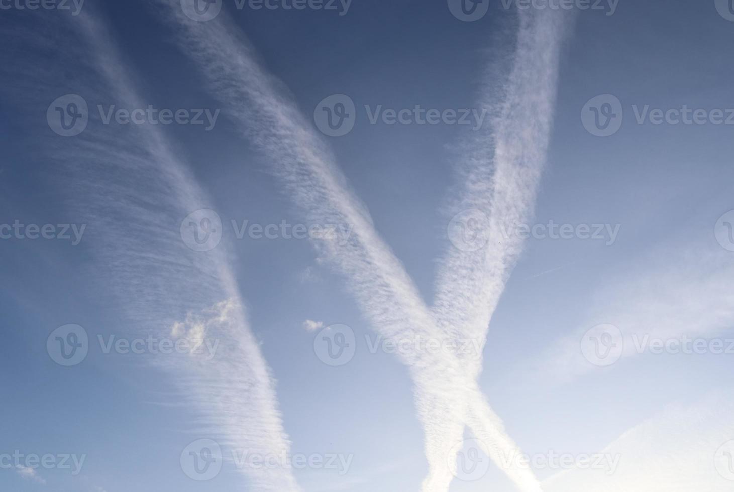 Aircraft condensation contrails in the blue sky inbetween some clouds photo