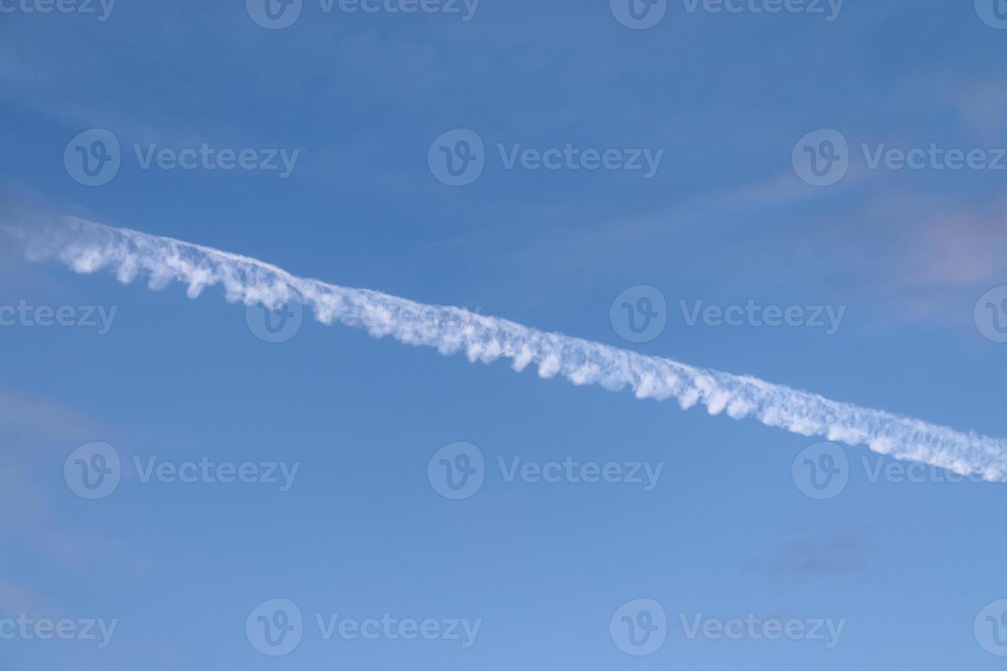 Aircraft condensation contrails in the blue sky inbetween some clouds photo