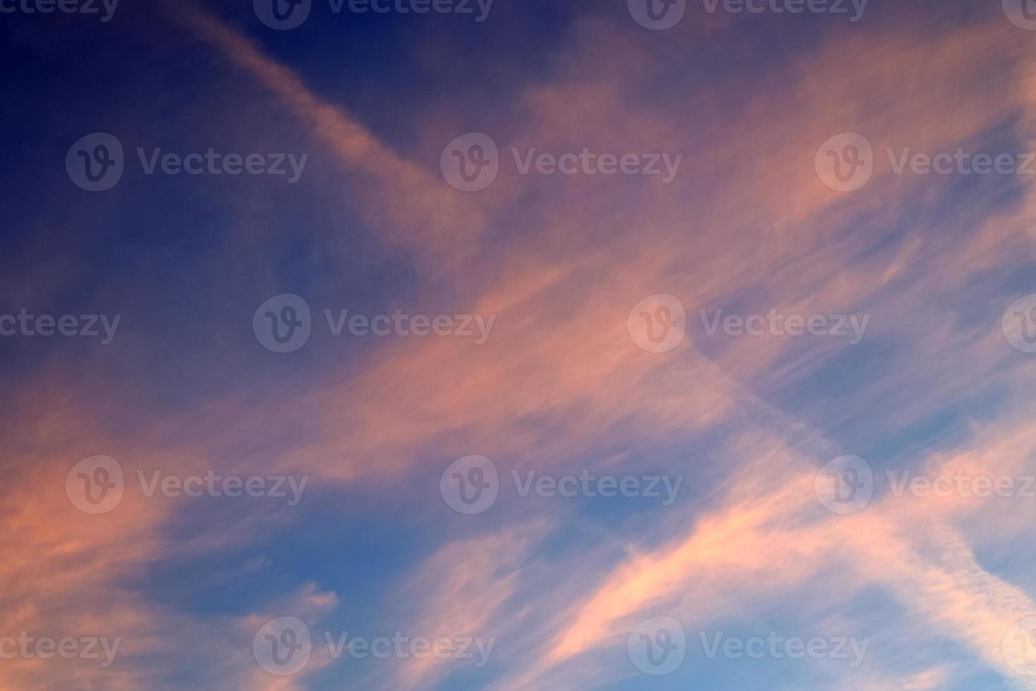 Aircraft condensation contrails in the blue sky inbetween some clouds photo