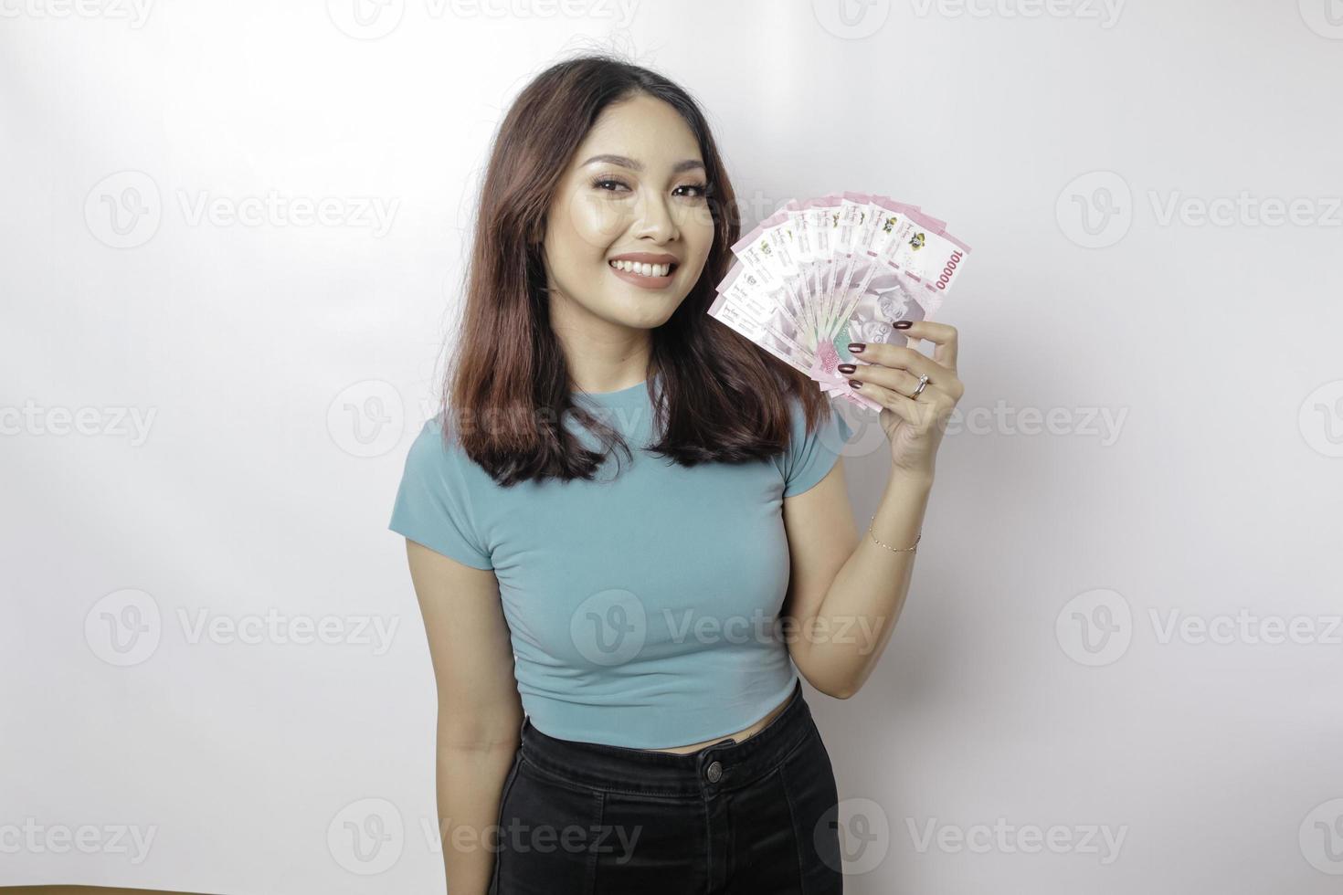 A happy young woman is wearing blue t-shirt and holding cash money in Indonesian rupiah isolated by white background photo