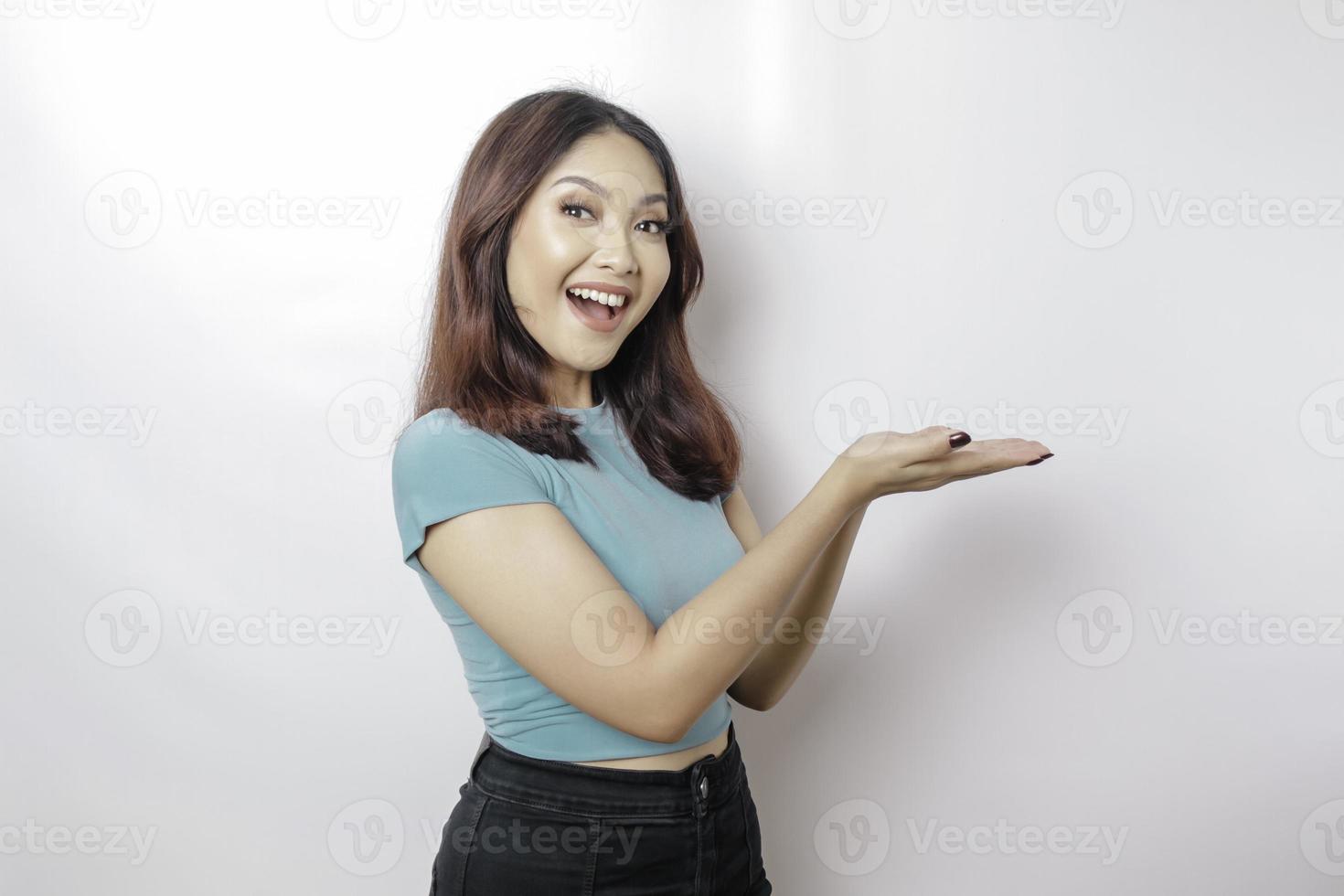 Excited Asian woman wearing blue t-shirt pointing at the copy space beside her, isolated by white background photo