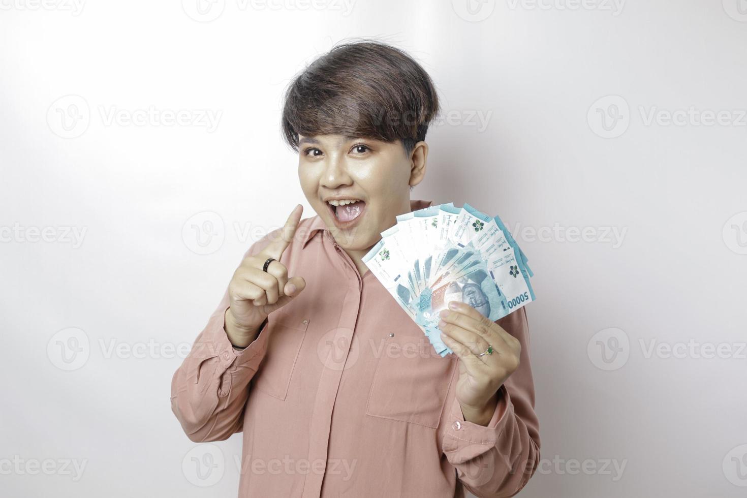 A happy young woman is wearing pink shirt and holding cash money in Indonesian rupiah isolated by white background photo