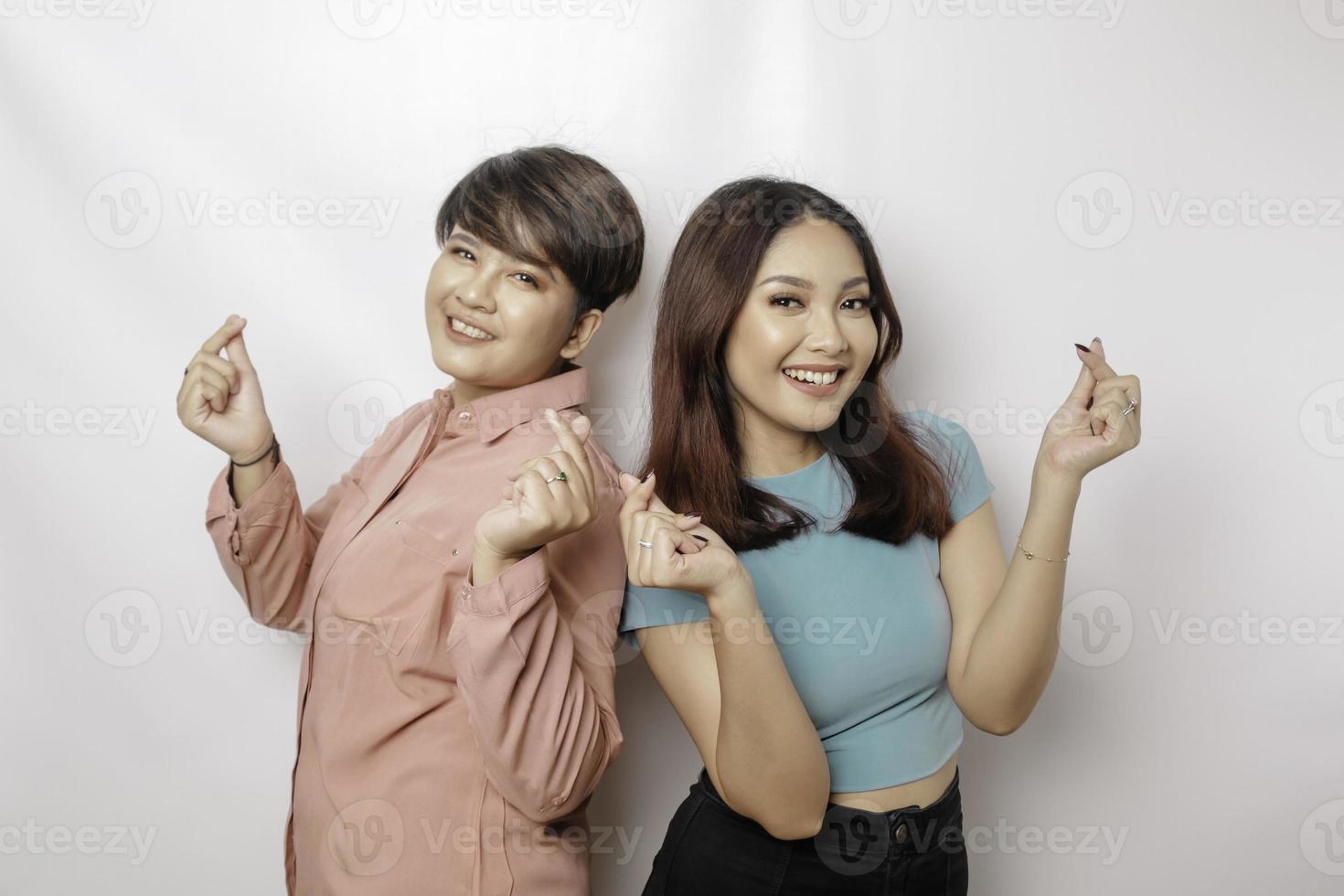 Two attractive young Asian women wearing blue and pink t-shirt feels happy and a romantic shapes heart gesture expresses tender feelings photo