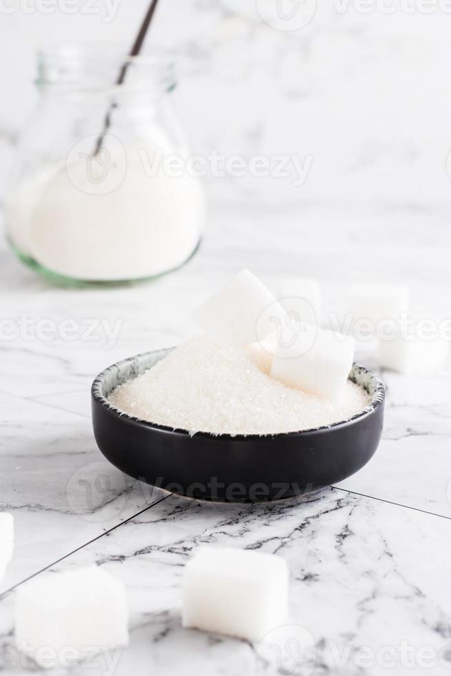 Granulated sugar and sugar cubes in a bowl and sugar in a jar on the table. Vertical view photo