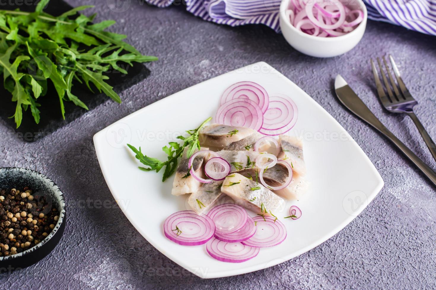 Sliced salted herring in oil with onion and dill on a plate on the table. Simple snack photo