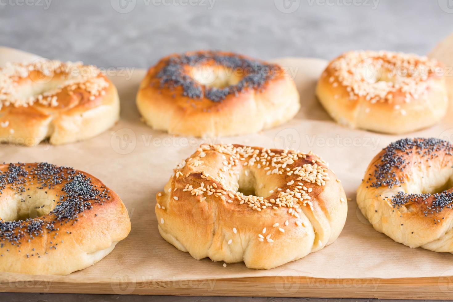 Baked bagels with poppy seeds and sesame seeds on parchment on the table. Homemade pastries photo