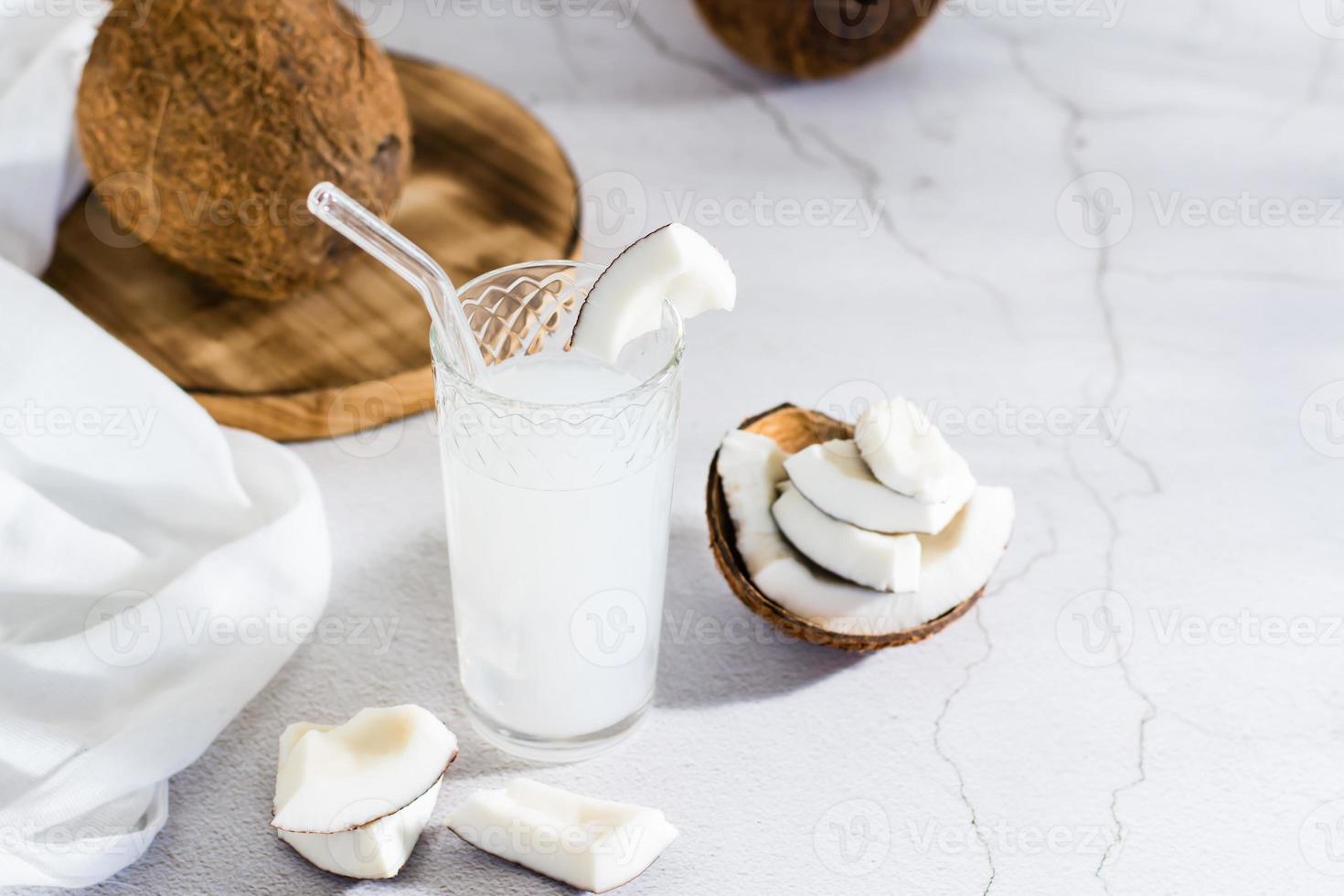 Coconut milk in a glass and pieces of tropical fruit on the table. Natural plant alternative photo