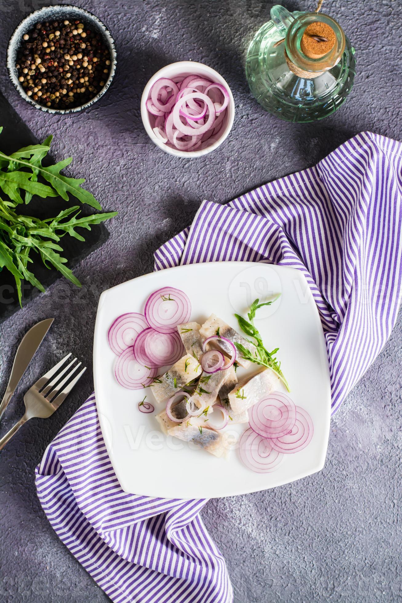 Sliced salted herring in oil with onion and dill on a plate. Simple