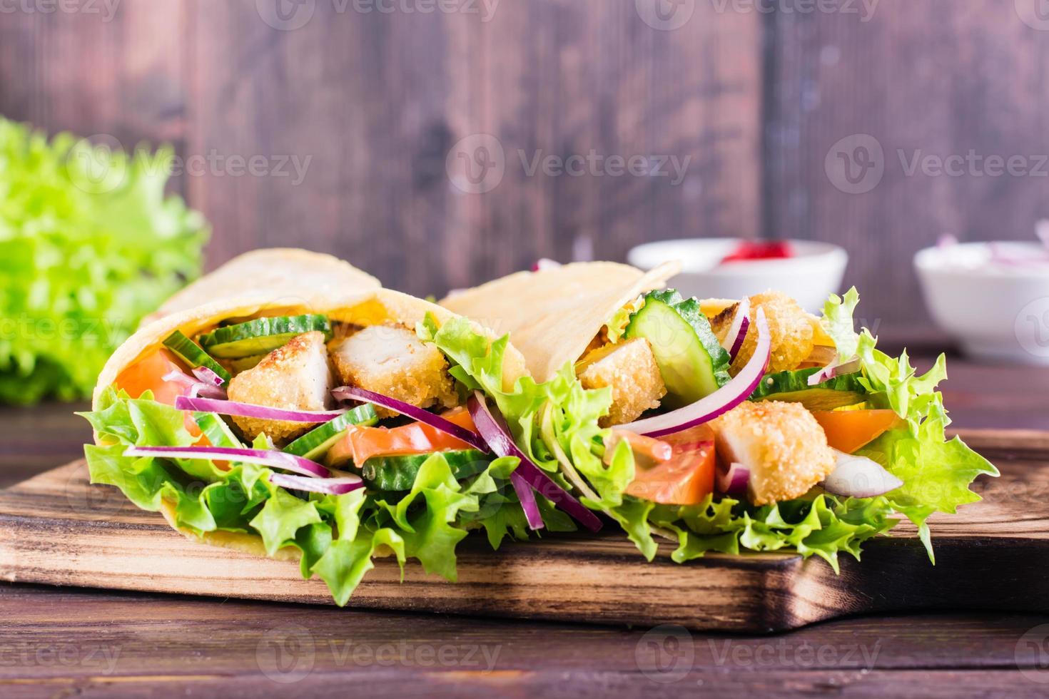 envolturas de tortilla mexicana con pollo y verduras en un tablero sobre la mesa. de cerca foto