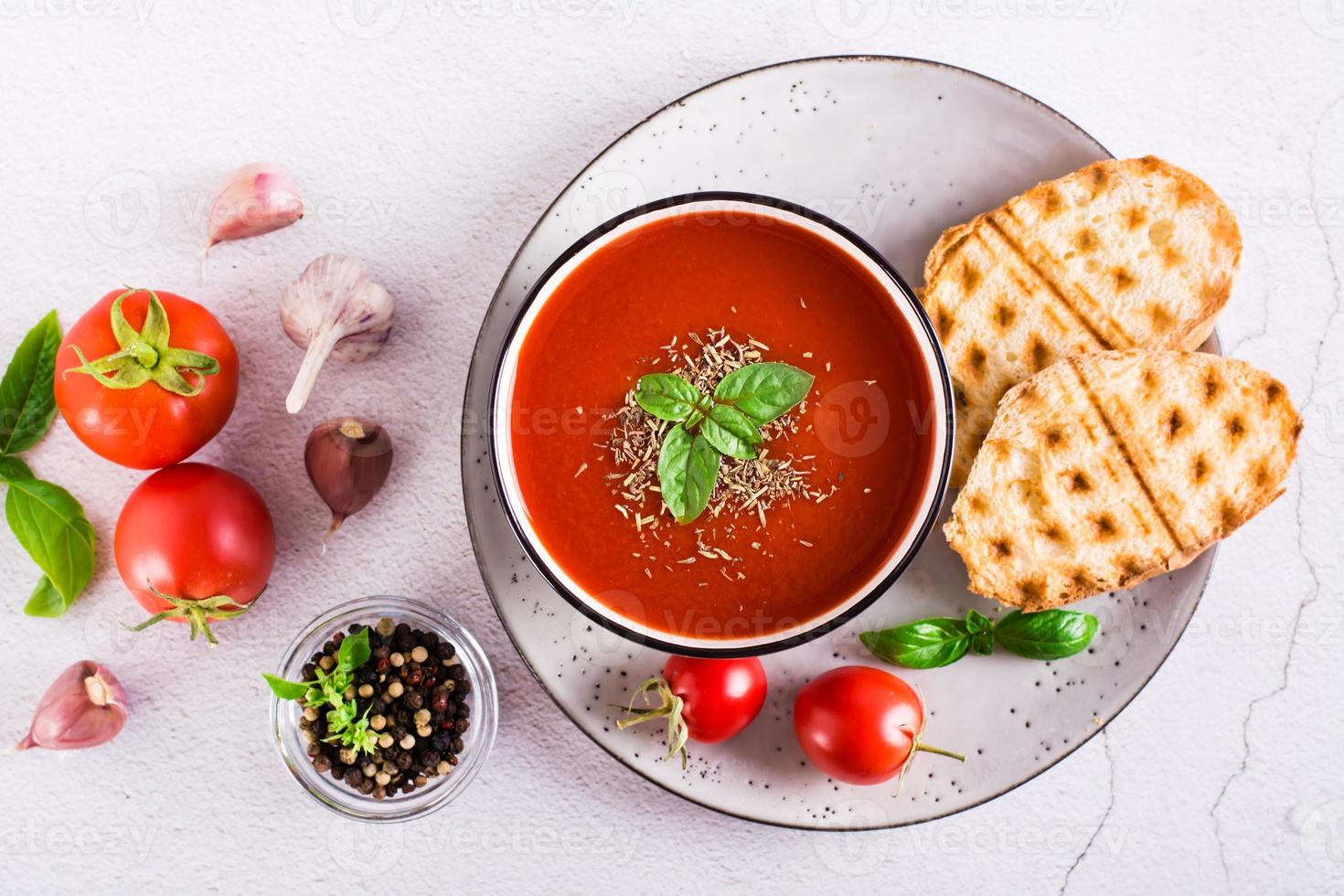 Fresh tomato soup with basil in a bowl and fresh vegetables on the table. Top view photo