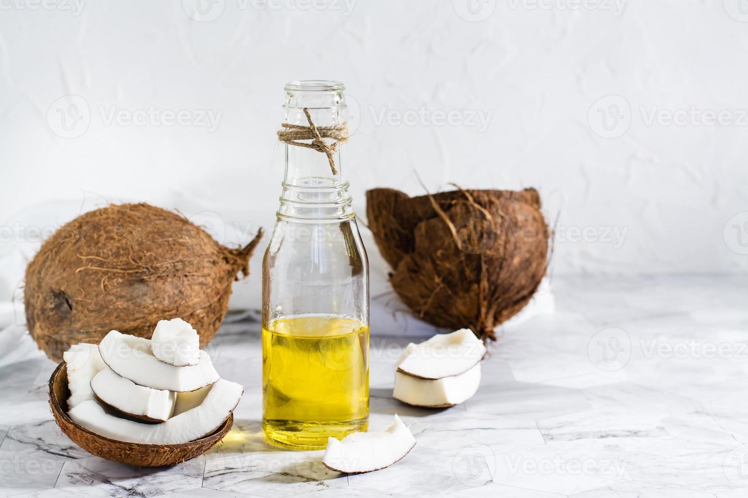 aceite de coco vegetal fresco en una botella y trozos de coco sobre la mesa. cosmética natural foto