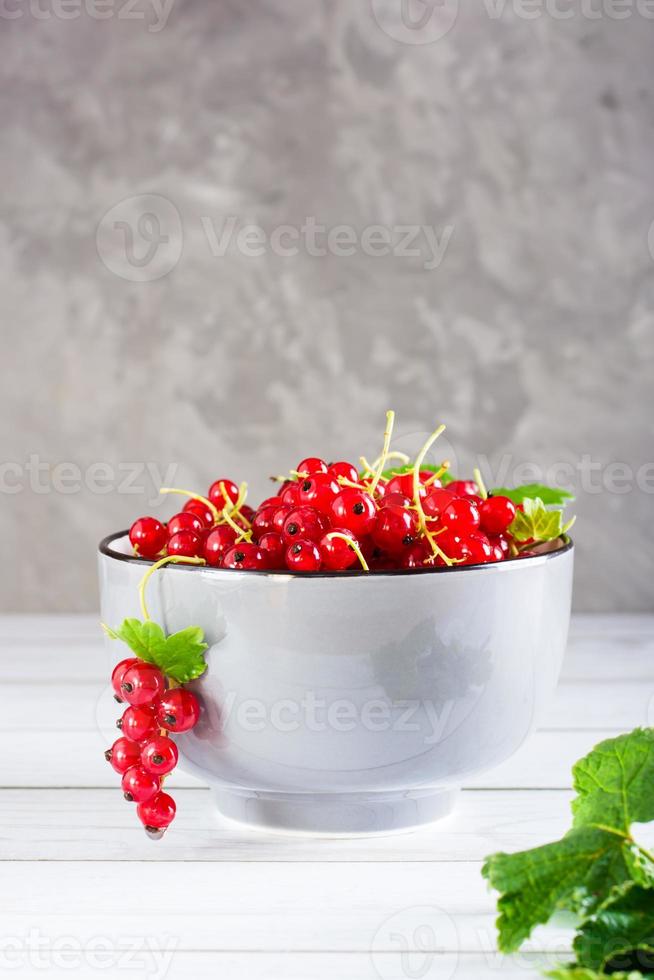 Fresh red currants in a bowl and leaves on the table. Organic summer food. Vertical view photo