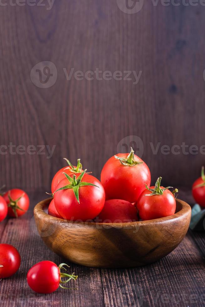 Organic ripe tomatoes in a bowl on a wooden table. Harvest and local products. Vertical view photo