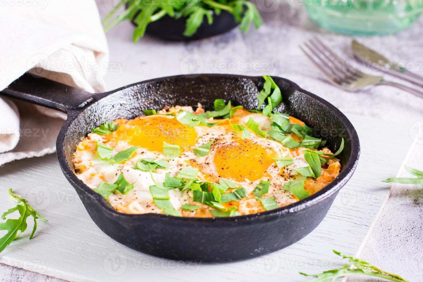 shakshuka con tomates y rúcula en una sartén sobre la mesa. plato tradicional mediterraneo foto