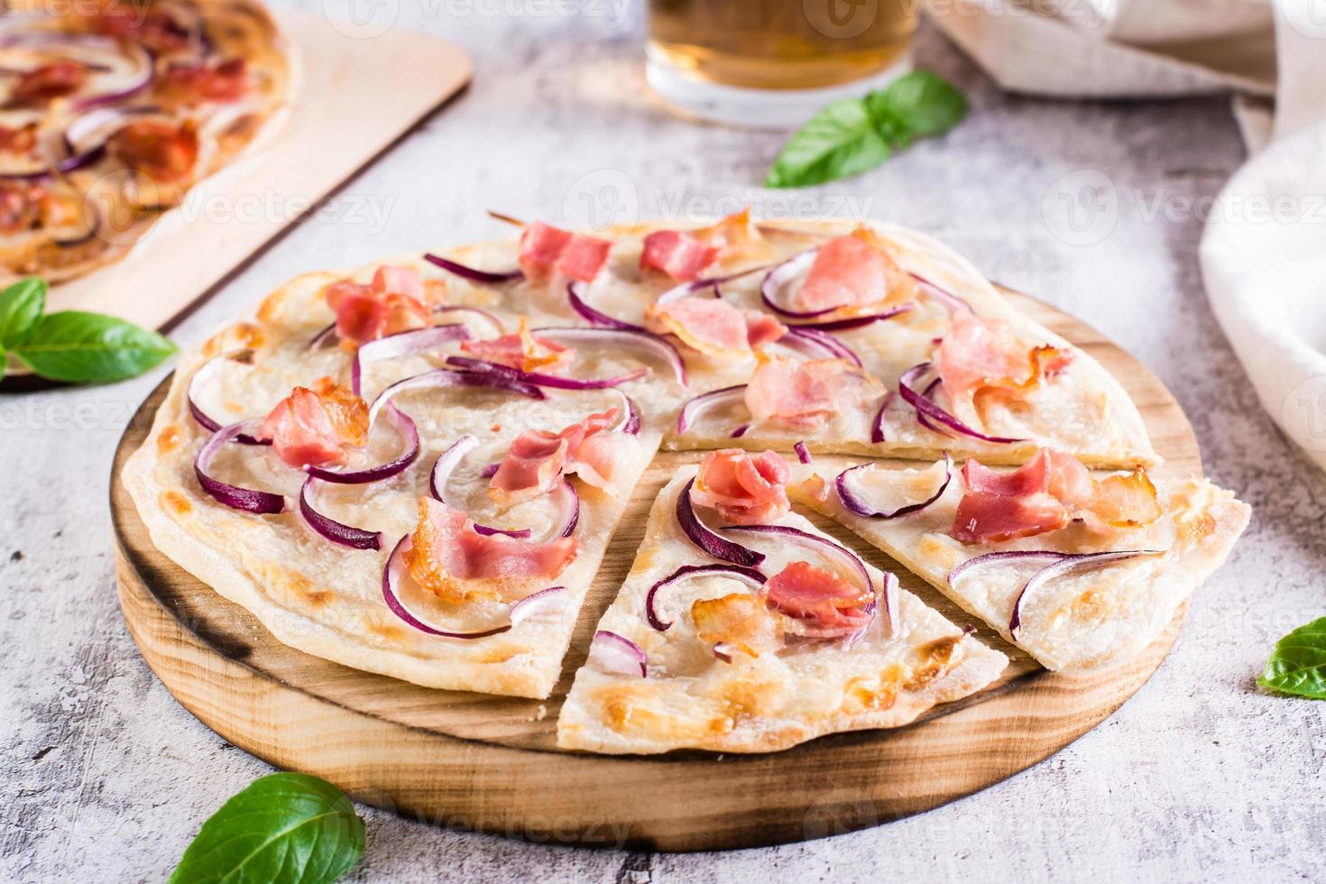 tarta francesa flammkuchen con queso crema, cebolla y tocino en un tablero sobre la mesa foto