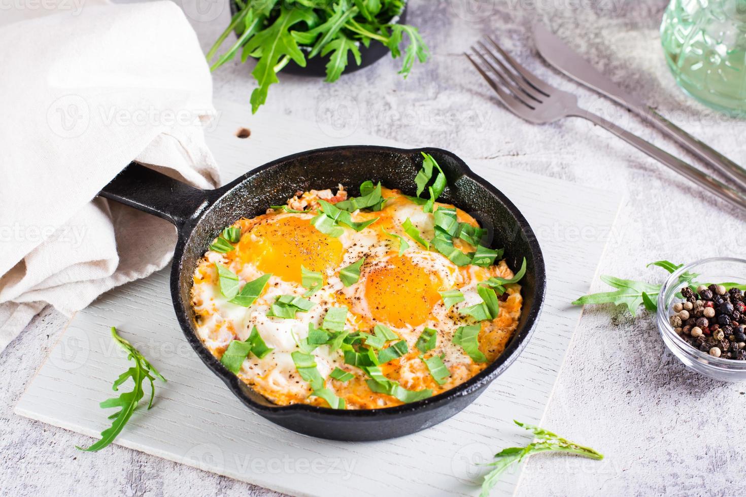 Shakshuka with poached eggs in spicy tomato pepper sauce and arugula in a frying pan on the table photo