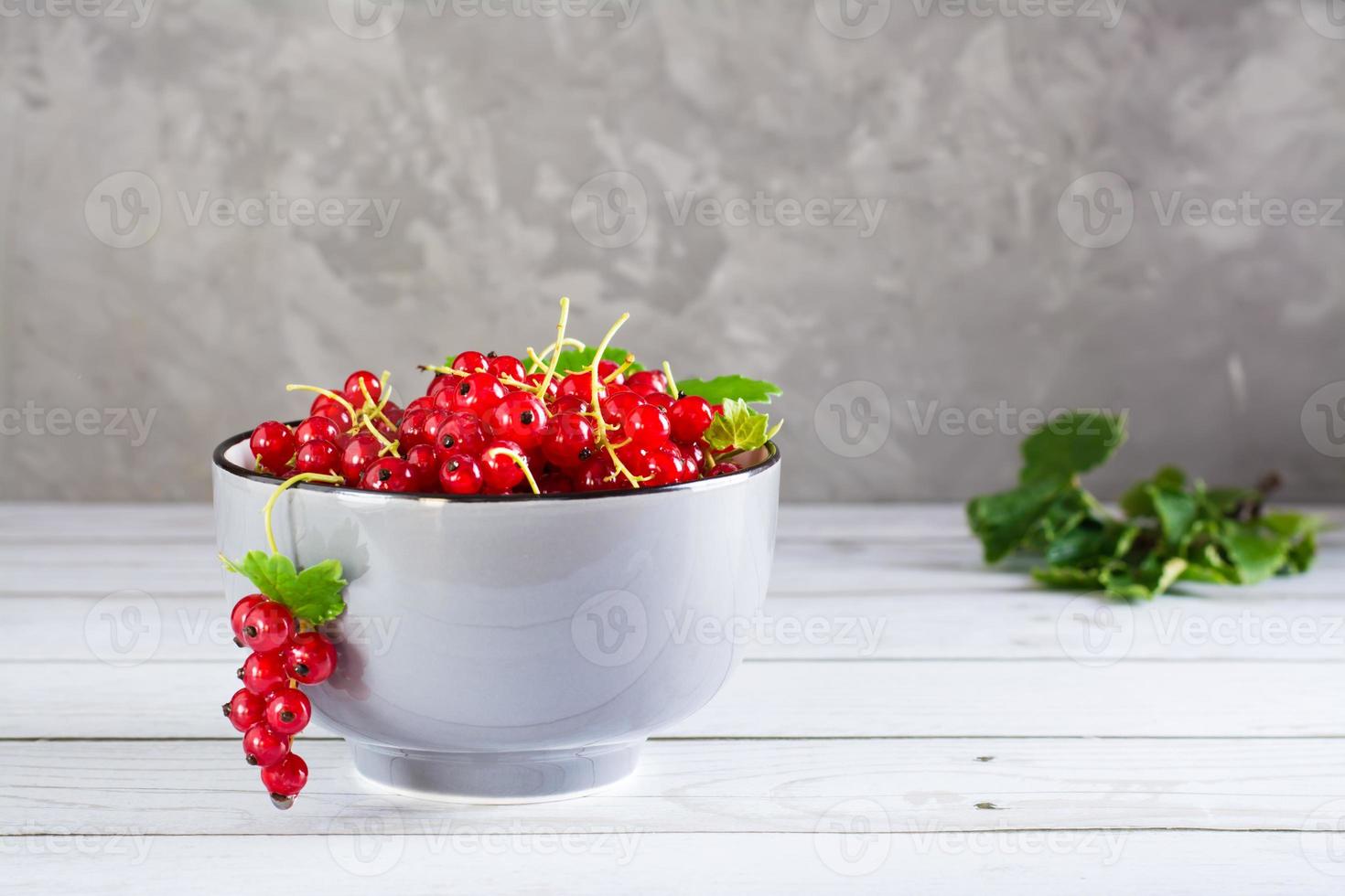 Fresh red currants in a bowl and leaves on the table. Organic summer food. photo