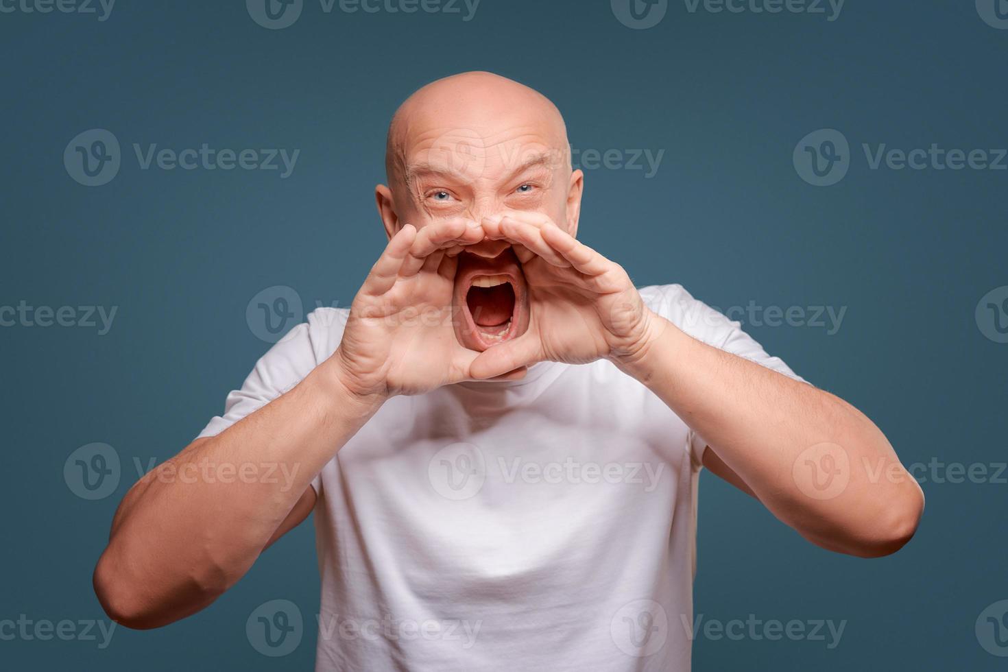 Handsome happy man wearing white T-shirt, guy speaking loudly, isolated on blue background photo