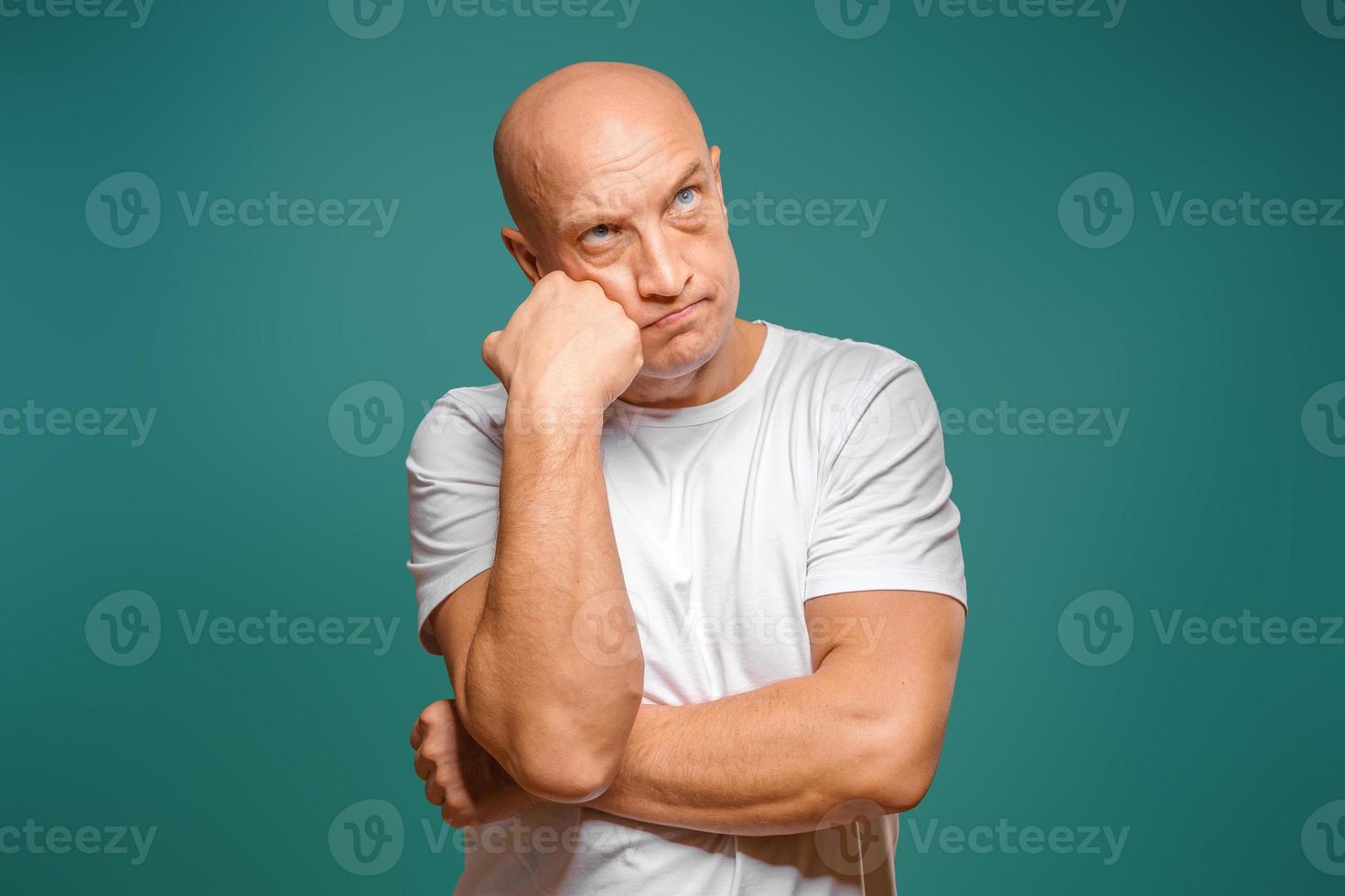 portrait of a bald man in a white t-shirt in the background, pensive expression, holding a finger near his temple photo