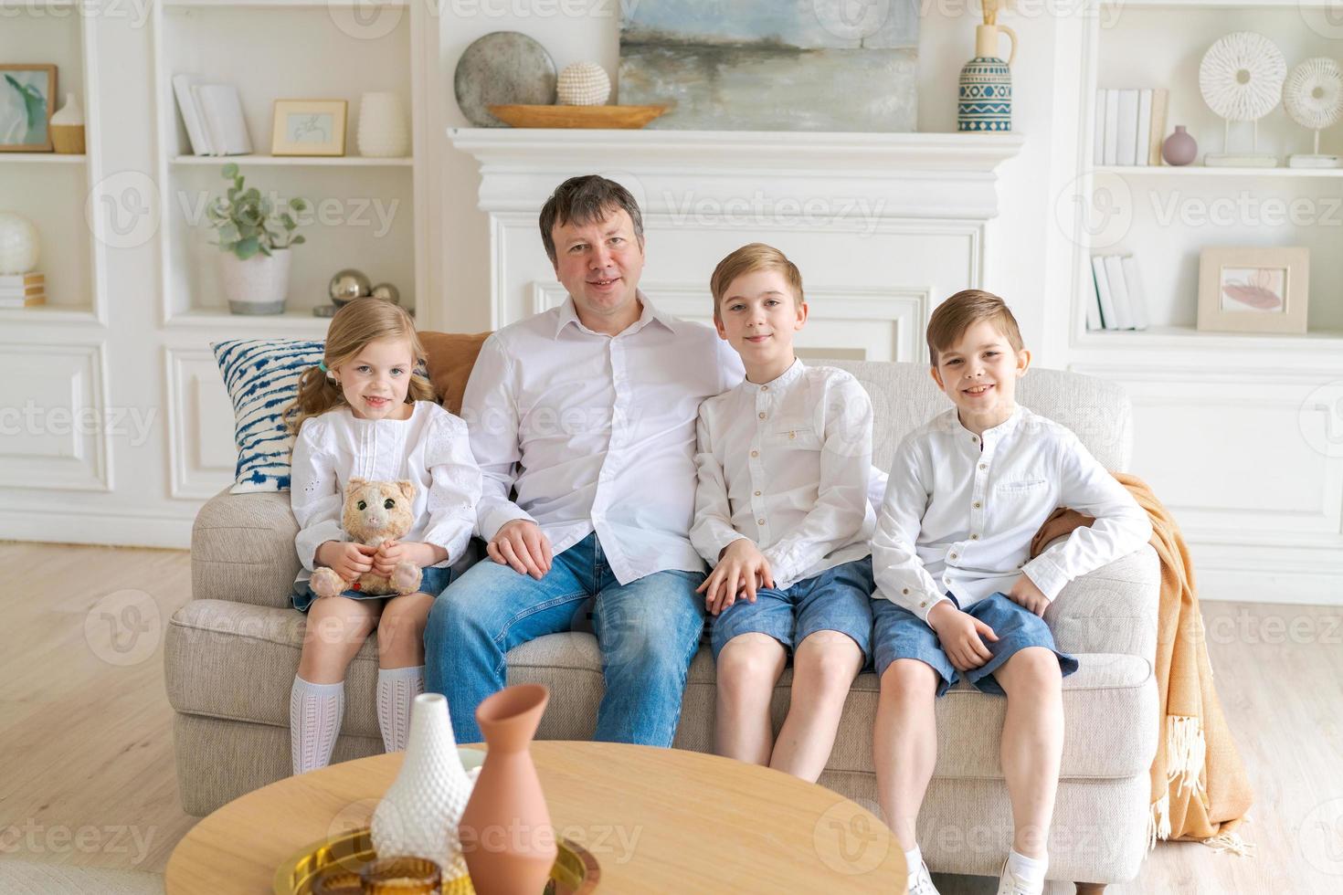 Happy father with three little children sitting on sofa looking at each other photo