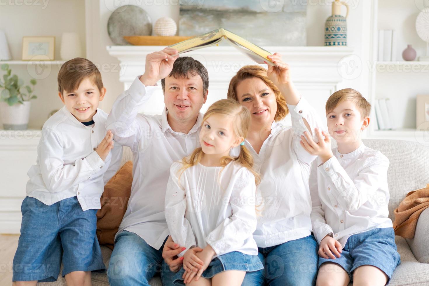 Happy family are sitting in new house in living room on couch holding book photo