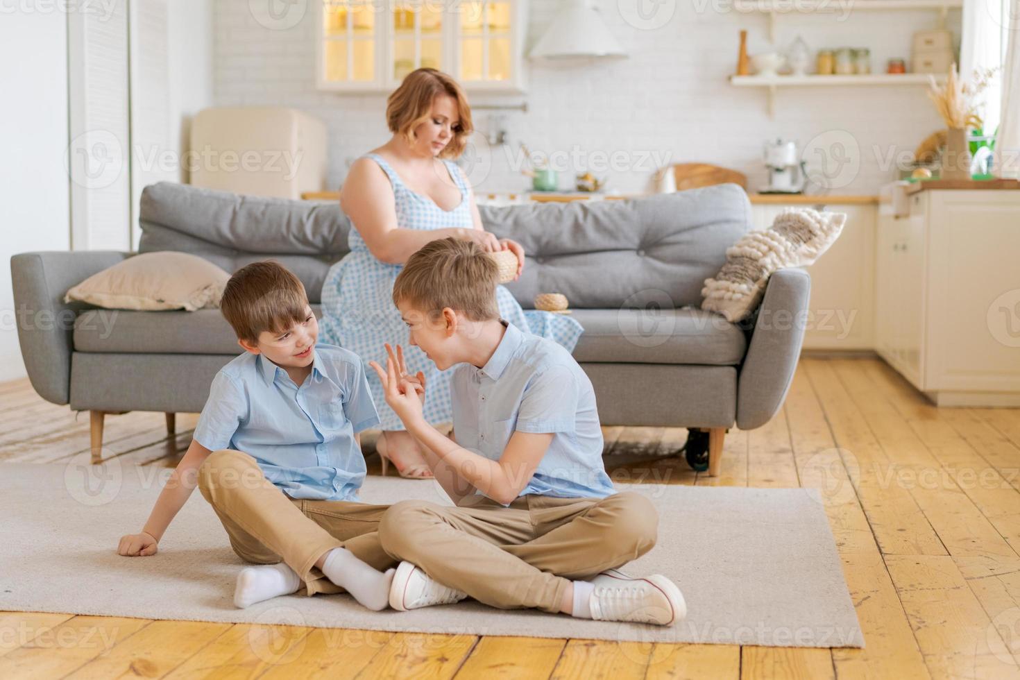 Children two brothers play together on floor, while young mother sits at home photo