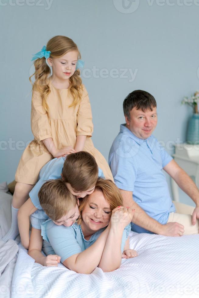 Happy young mother lies on bed in chaos with three young children, two wild photo