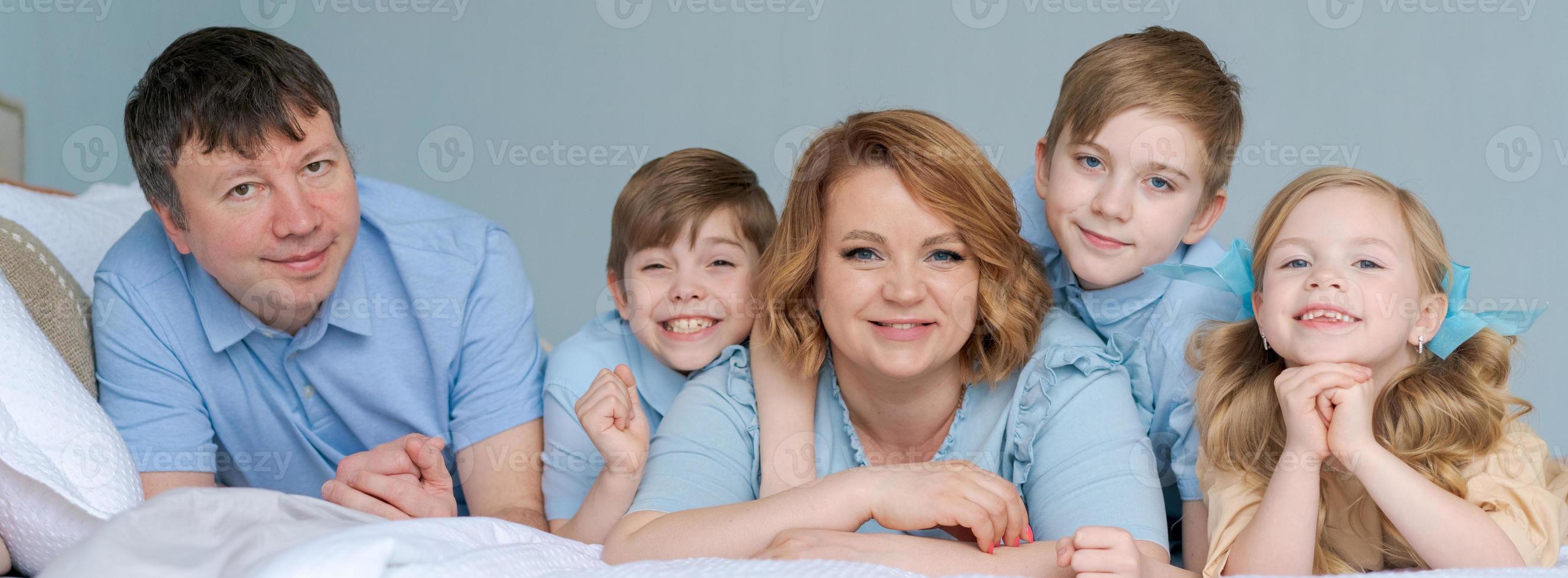 feliz gran familia caucásica se acuesta en el dormitorio en la cama y sonríe. vestida de azul foto