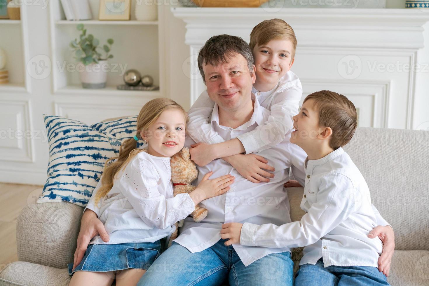 Happy father with three little children sitting on sofa looking at each other photo