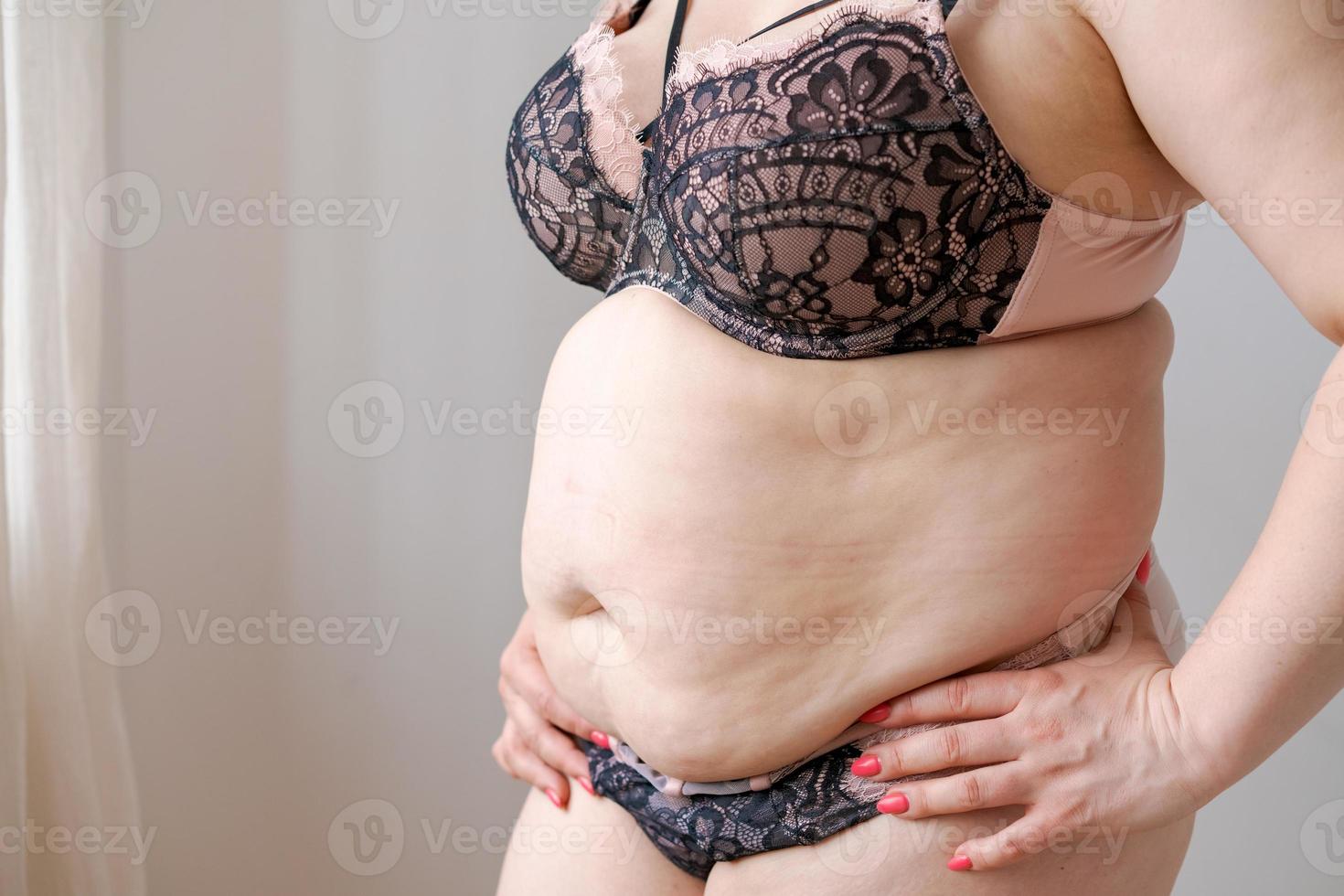 Obese plump caucasian young woman, girl holding her belly by hand, shows excess photo