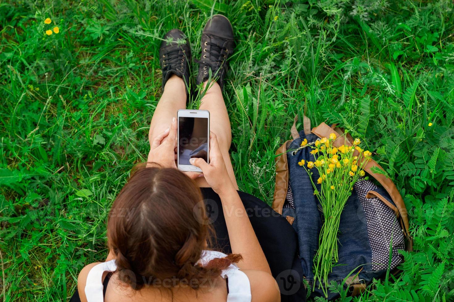 mujer sentada en la hierba verde con el teléfono en la vista superior de la mano foto