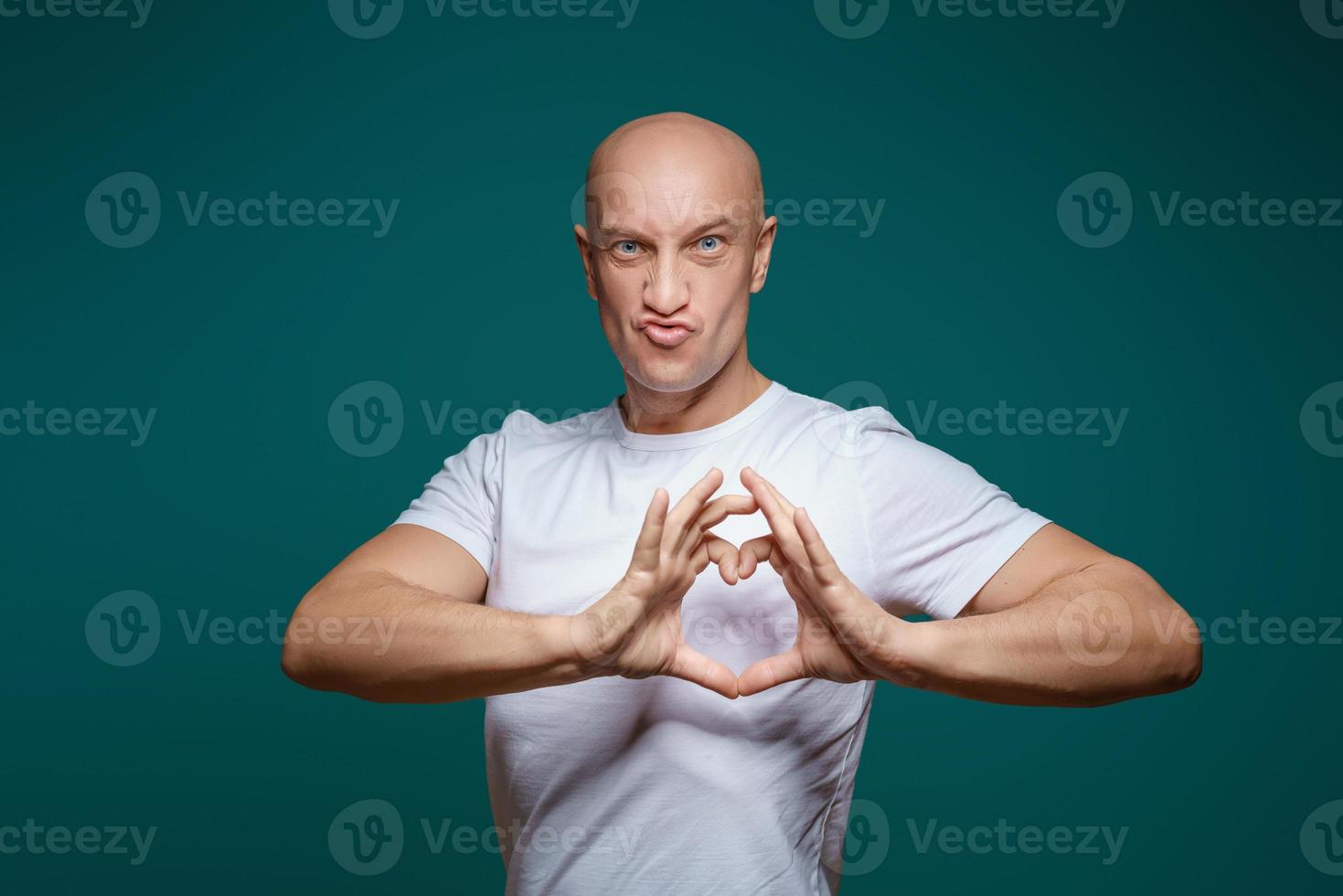 Portrait of a bald man smiling and holding hands in the shape of a heart, on a blue background . The concept of romance photo