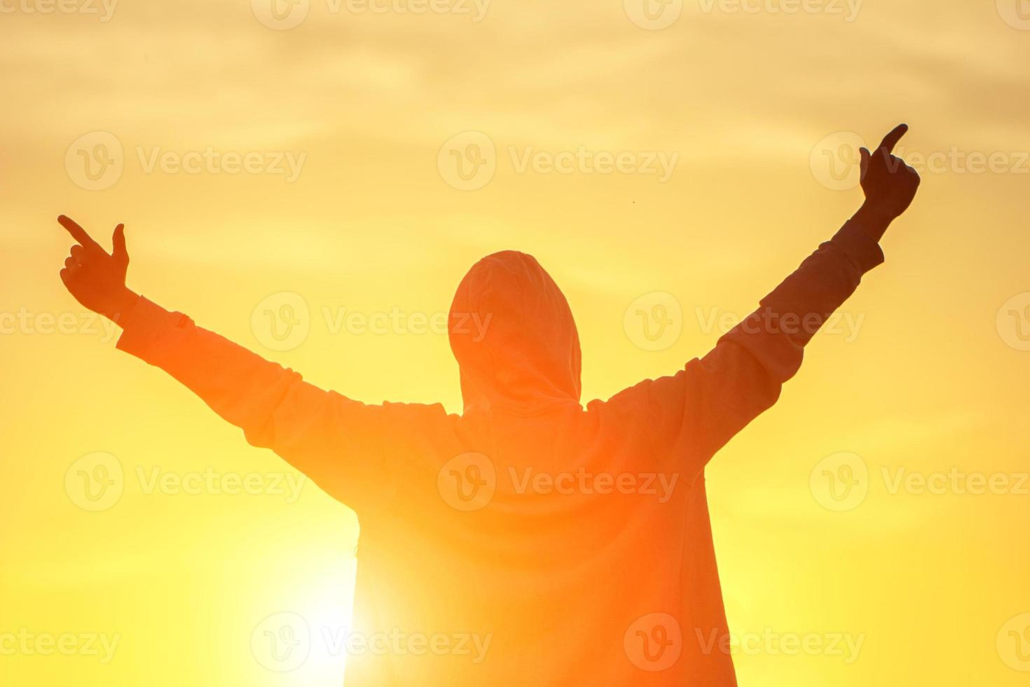 un hombre a la luz de la puesta de sol con las manos en alto, el concepto de éxito, libertad y alegría foto