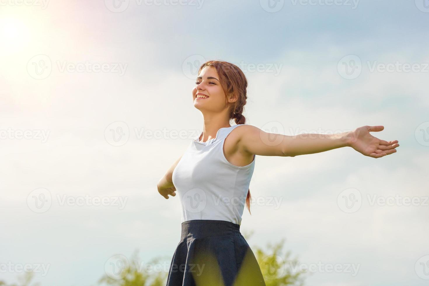 bella chica disfrutando del sol con los brazos extendidos en el campo contra el cielo foto