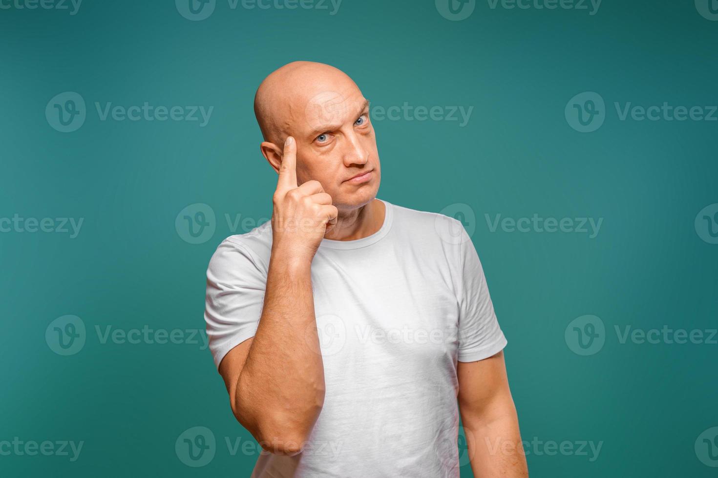 portrait of a bald man in a white t-shirt in the background, pensive expression, holding a finger near his temple photo