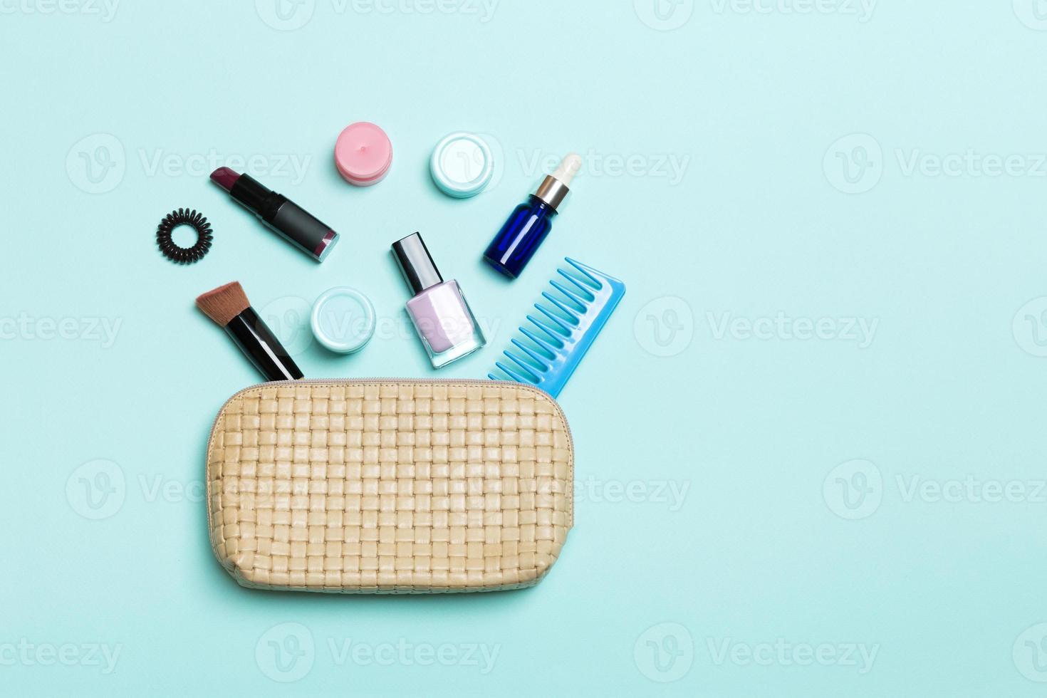 Top view of set of make up and skin care products spilling out of cosmetics bag on blue background. Beauty concept photo