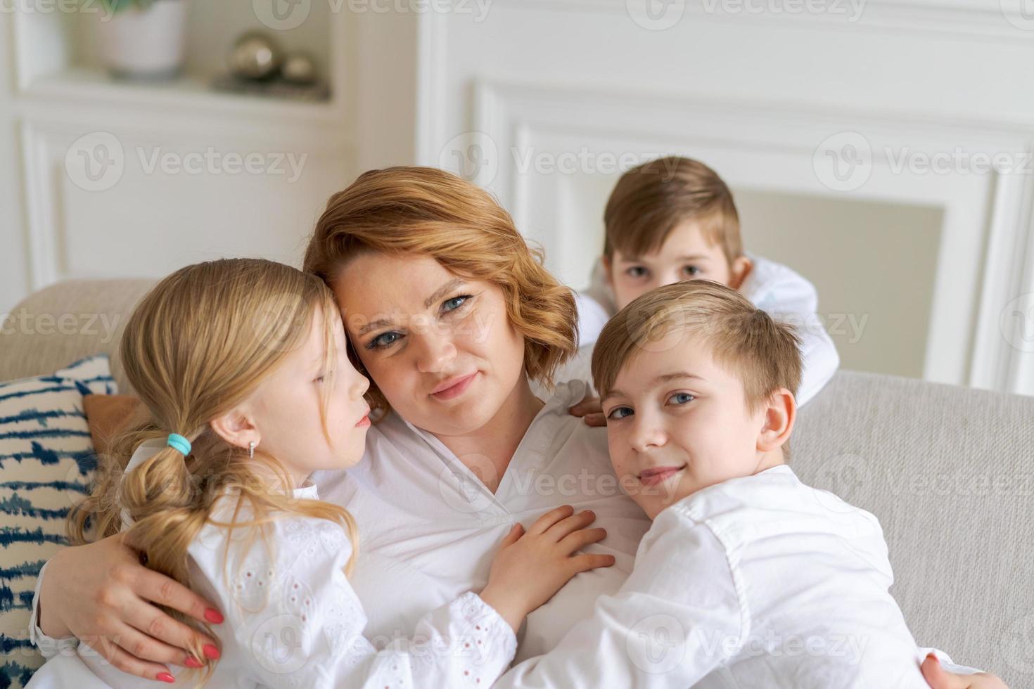 We love you. Smiling young woman, kids hug mom while sitting on sofa in living photo