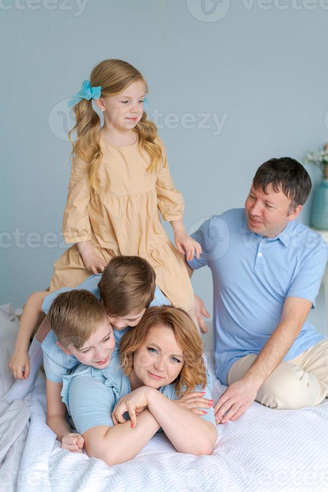 feliz joven madre yace en la cama en el caos con tres niños pequeños, dos salvajes foto
