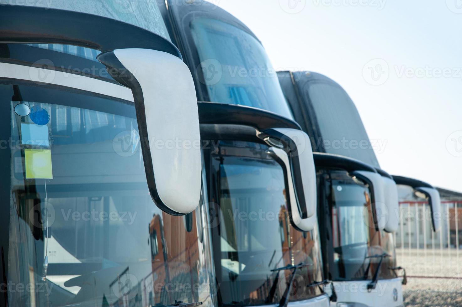 A passenger shift buses stand in a row on a construction site. Windshields photo