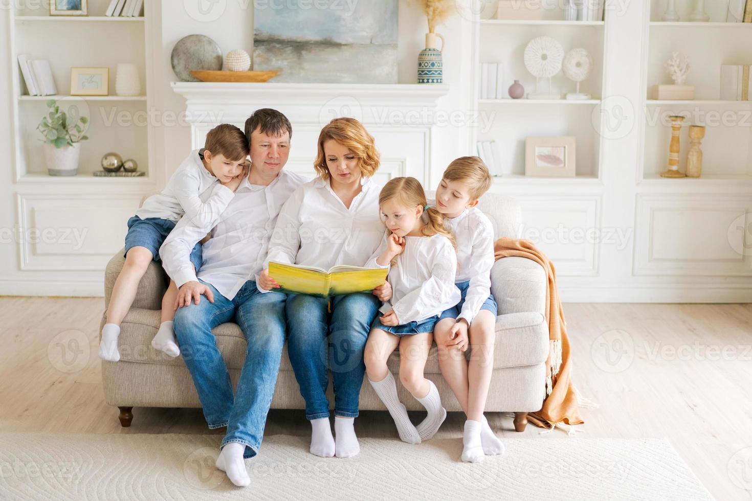 libro de lectura familiar feliz en casa. mamá, papá y niños pequeños se sientan juntos foto