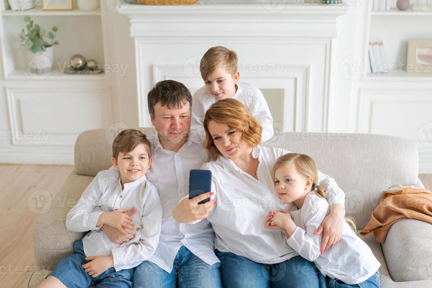 Happy parents with three kids using smartphone at home together sitting on cozy photo