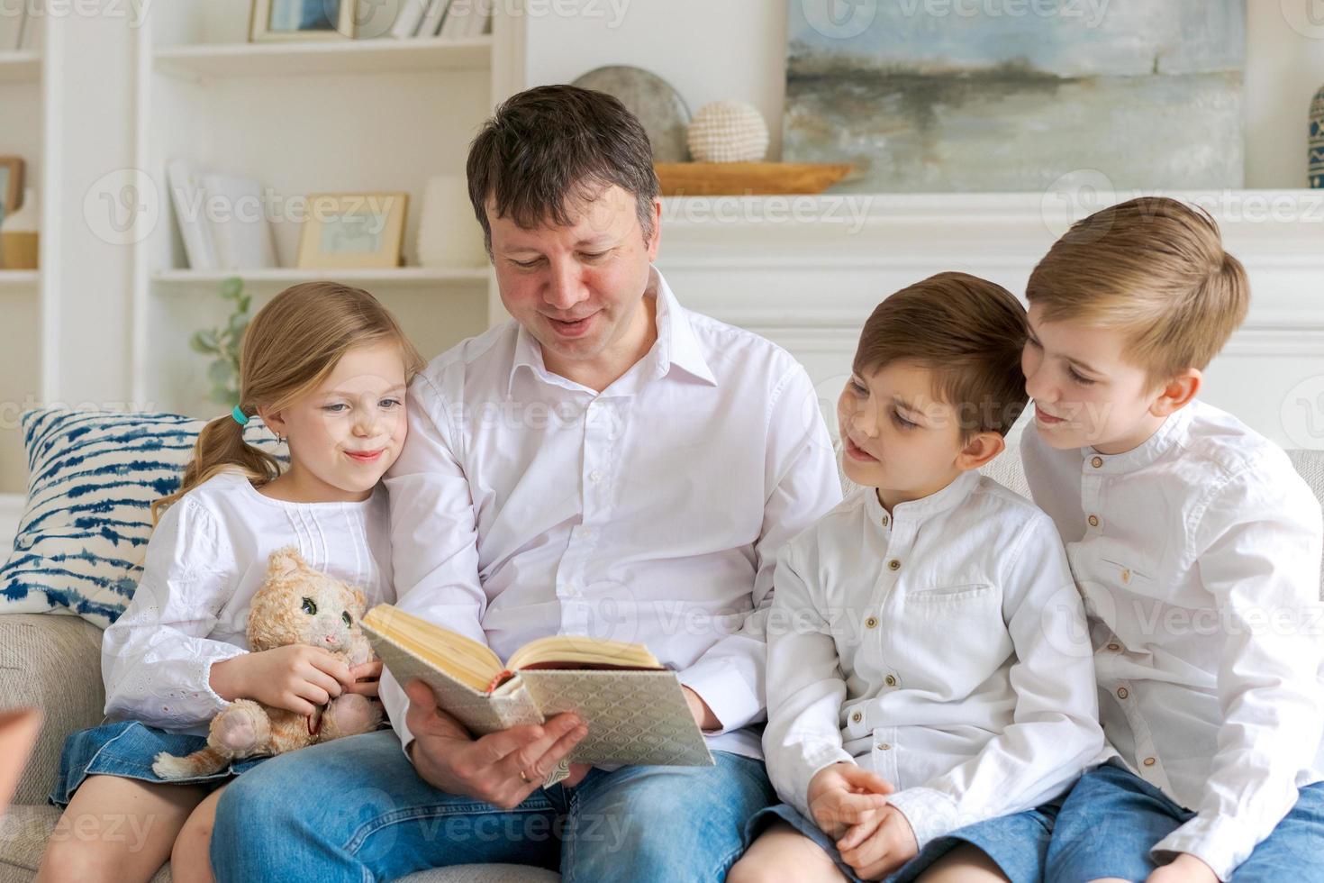 Cheerful dad with children are sitting on couch and reading book, preschoolers photo