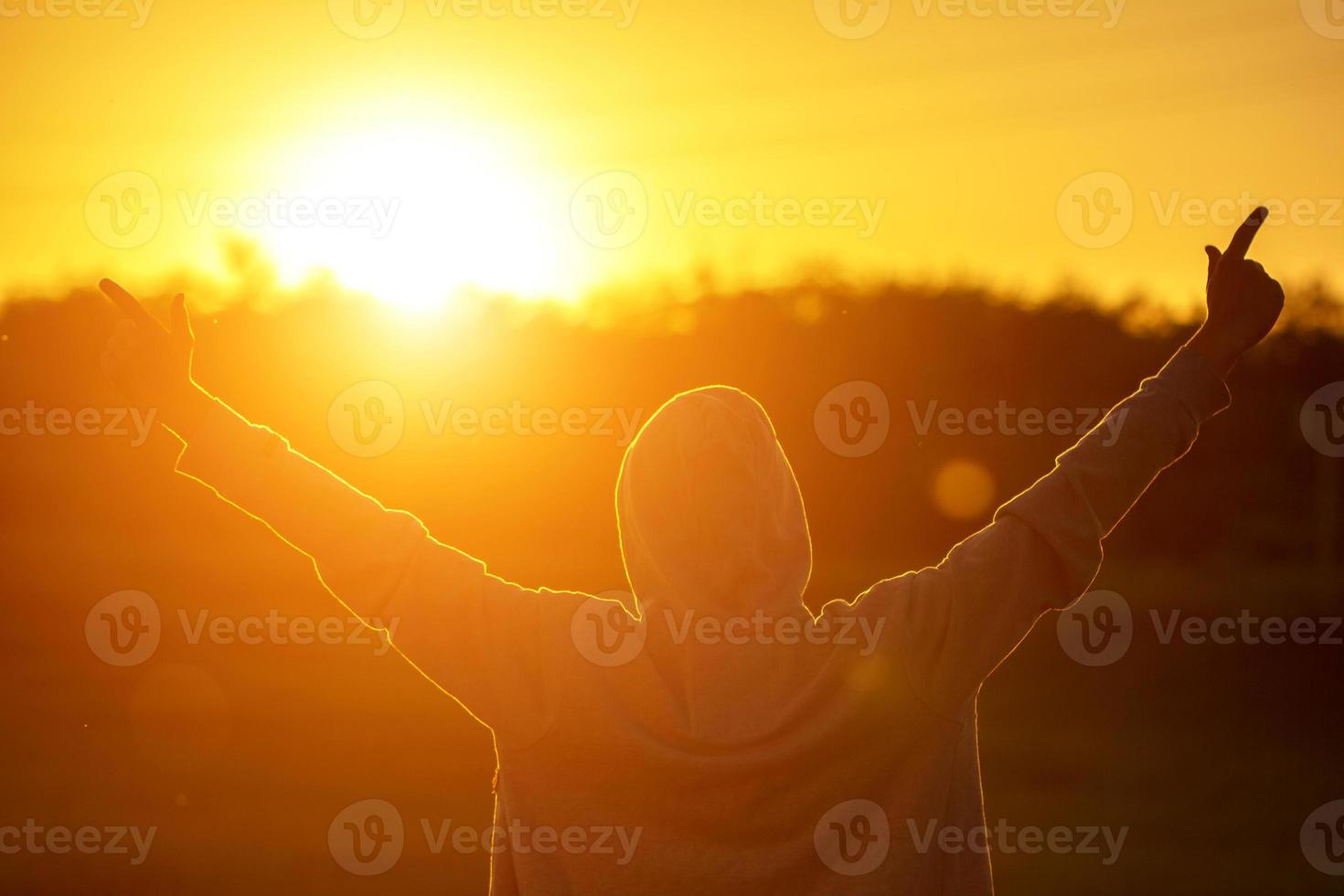 un hombre a la luz de la puesta de sol con las manos en alto, el concepto de éxito, libertad y alegría foto