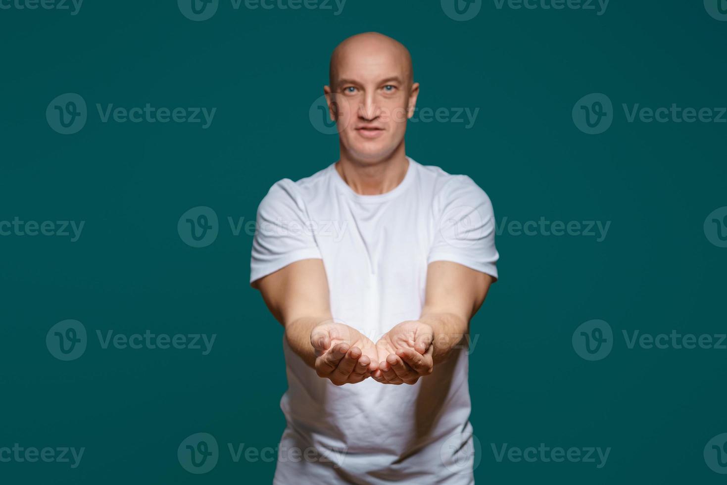 The bald man smiles and holds his hands in front of him, palms up, against a blue background photo
