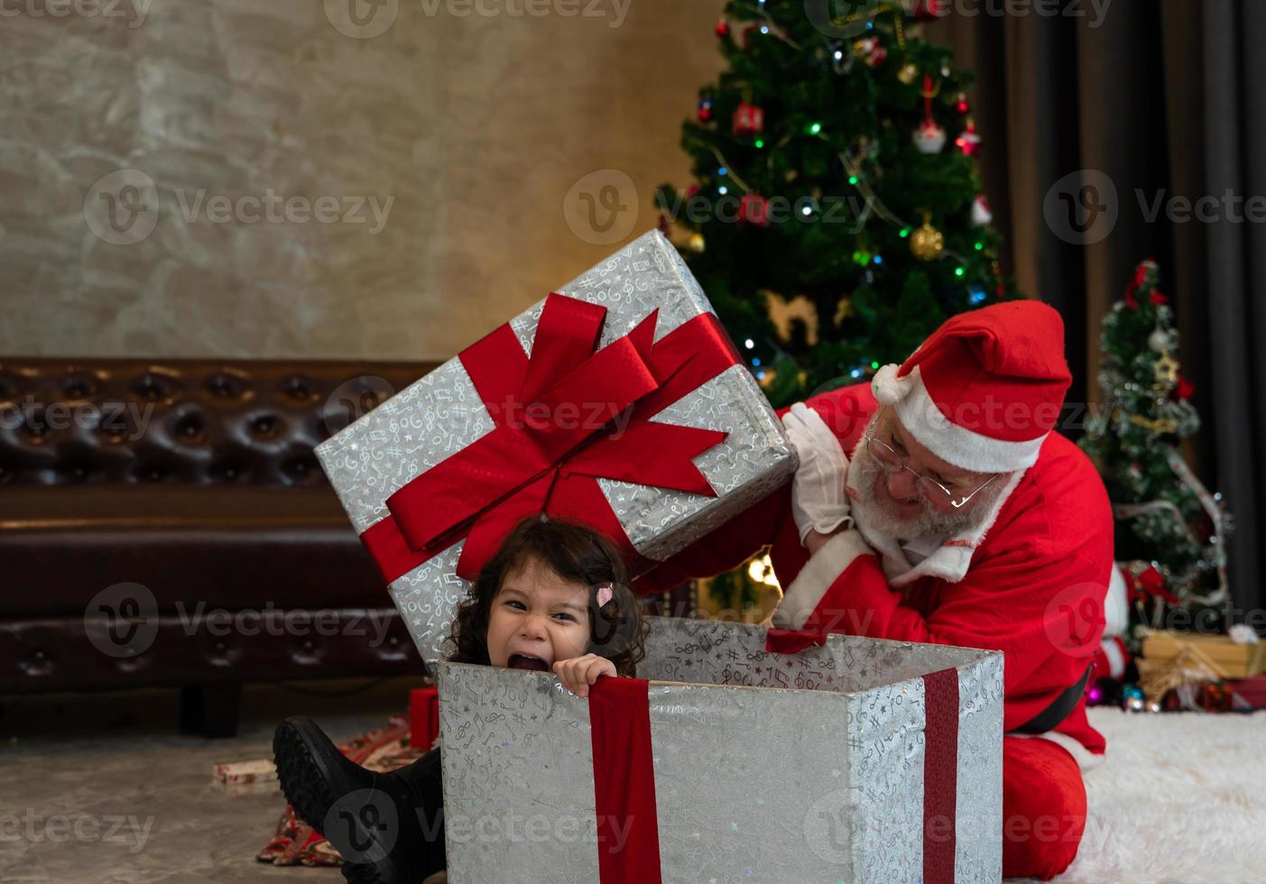 Kid girl siiting in large gift box while playing with Santa claus.  Celebrate holiday Christmas  and Thanksgiving party. photo