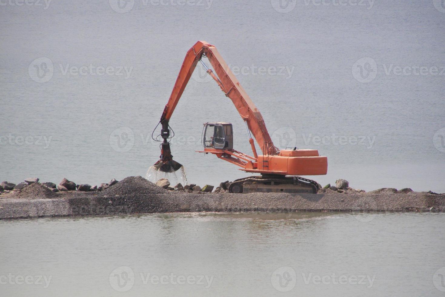 la grúa se encuentra en la costa artificial y vierte arena en la orilla del río artificial. foto