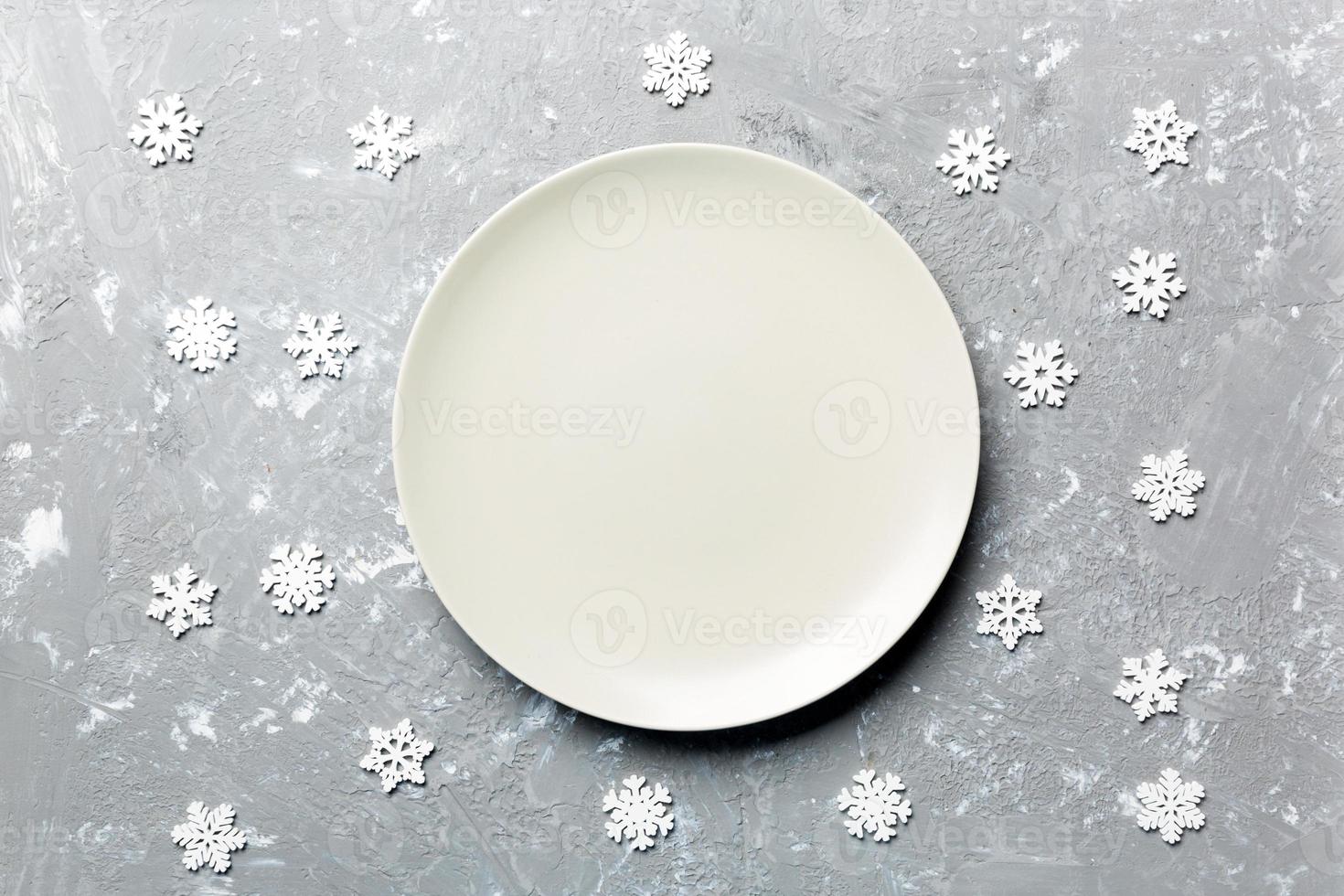 Top view of empty plate surrounded with snowflakes on cement background. New Year dinner concept photo