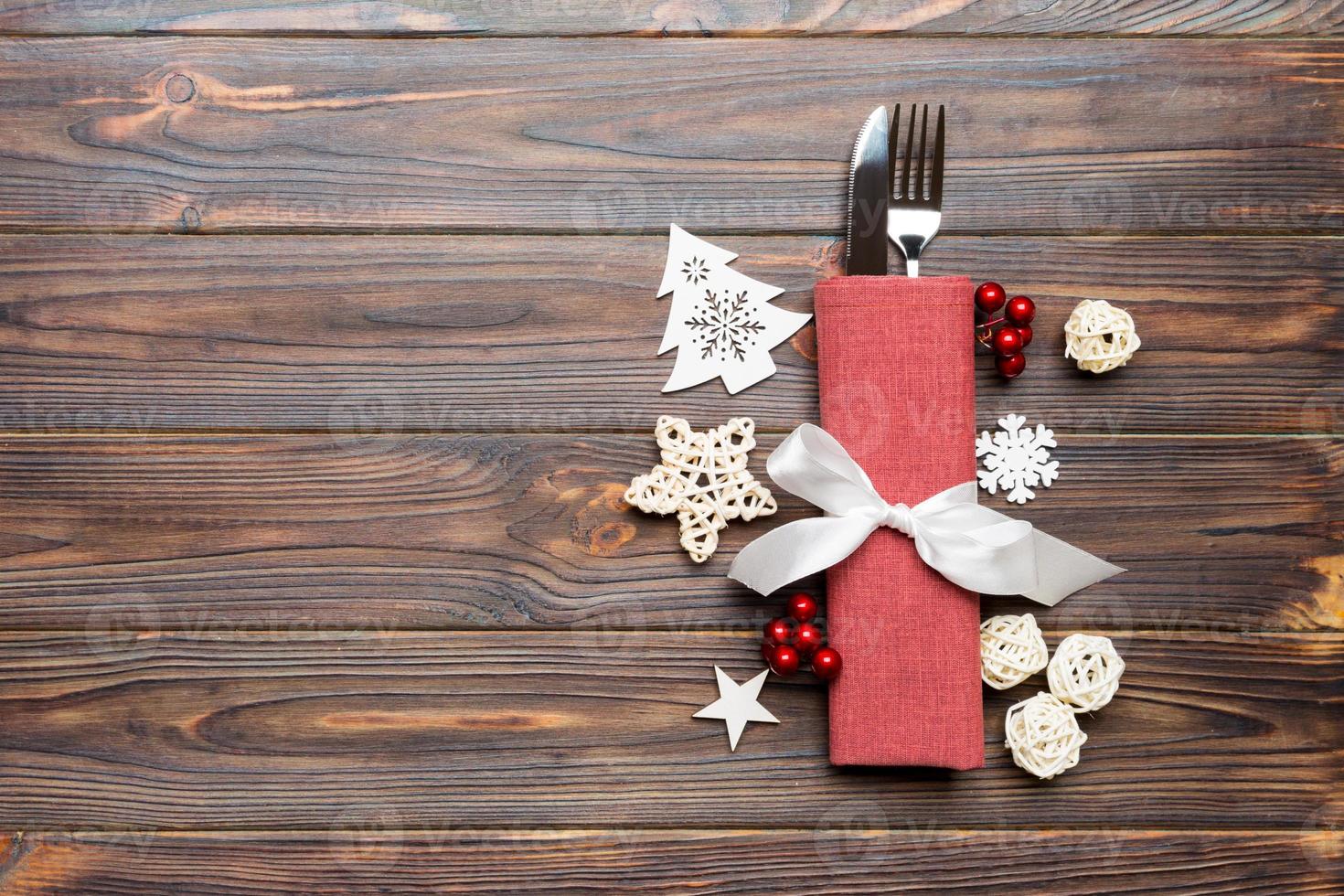 Top view of fork and knife on napkin on wooden background. Different christmas decorations and toys. New Year dinner concept with empty space for your design photo